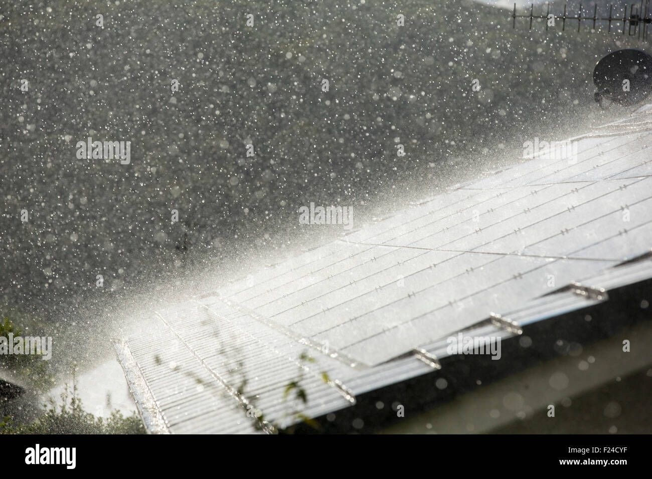 Un aguacero torrencial lluvia retroiluminada por Sun en una casa construida en el techo con paneles solares en Ambleside, Lake District, en el Reino Unido. Foto de stock