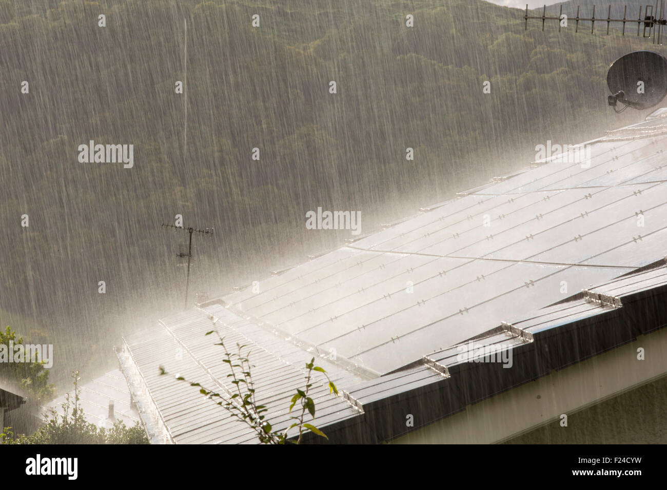Un aguacero torrencial lluvia retroiluminada por Sun en una casa construida en el techo con paneles solares en Ambleside, Lake District, en el Reino Unido. Foto de stock