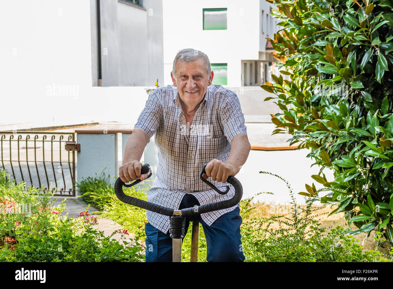 Ancianos varones octogenario mantiene en forma haciendo ejercicio en bicicleta en el jardín de la casa Foto de stock