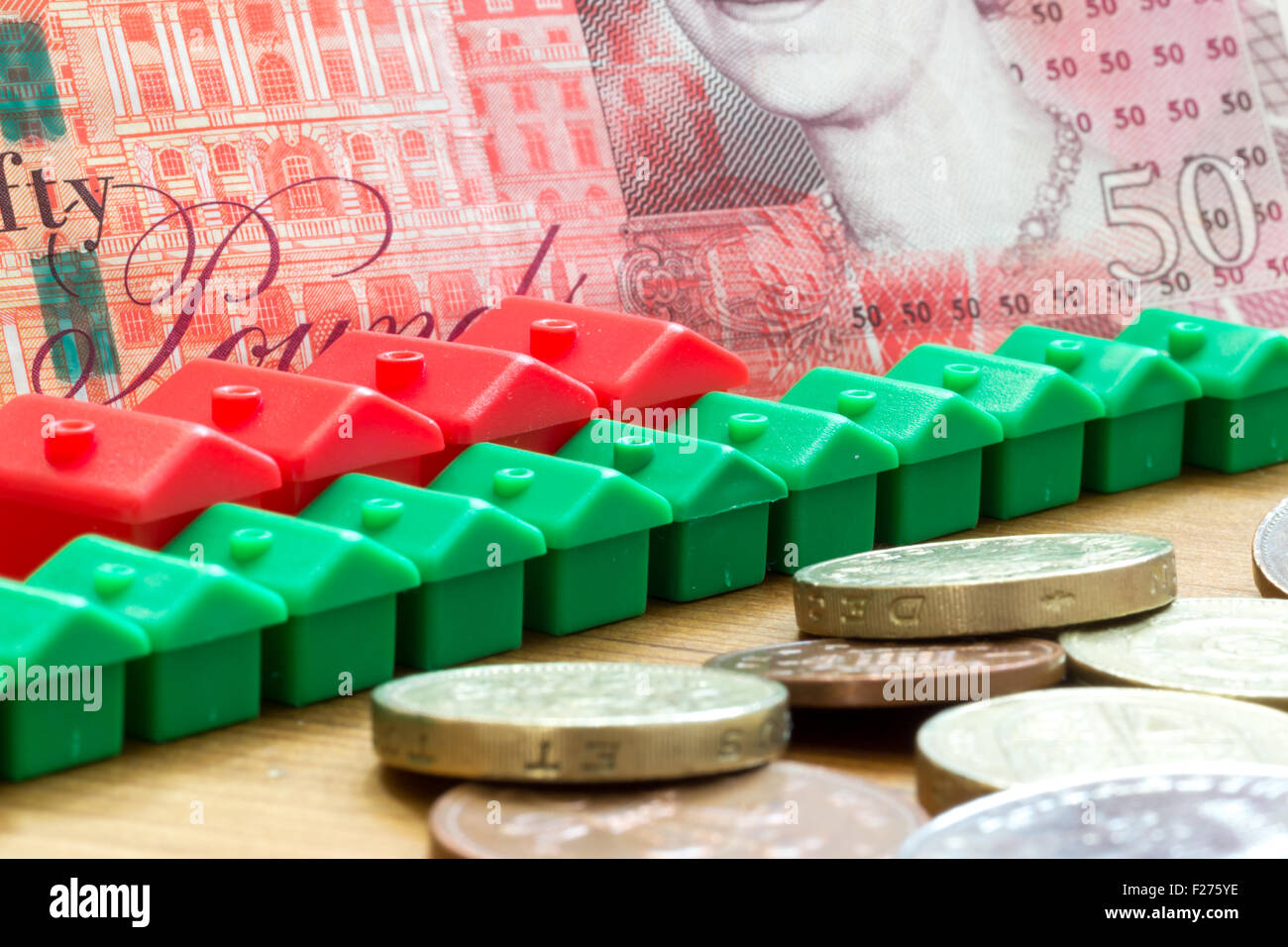 Verde y rojo imitación de plástico modelo casas forman una fila diagonal dinámica con un solo cincuenta libras británicas Bank note en la espalda Foto de stock