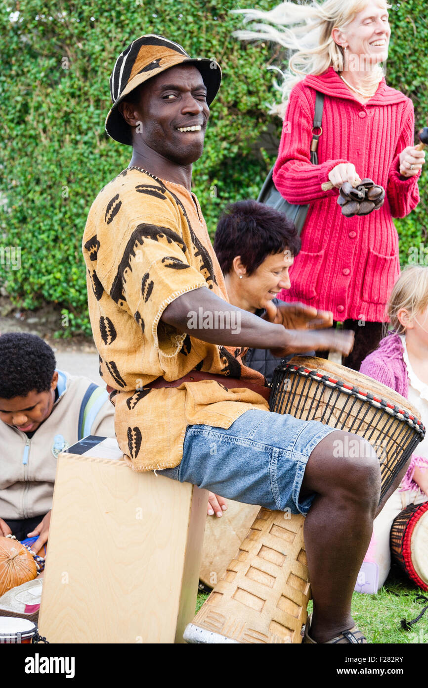 El hombre africano negro en pantalones cortos, camiseta y sombrero sentado  tocando el tambor bongo piscina sat evento en Inglaterra. Gran sonrisa,  eye-contact. Vista lateral Fotografía de stock - Alamy