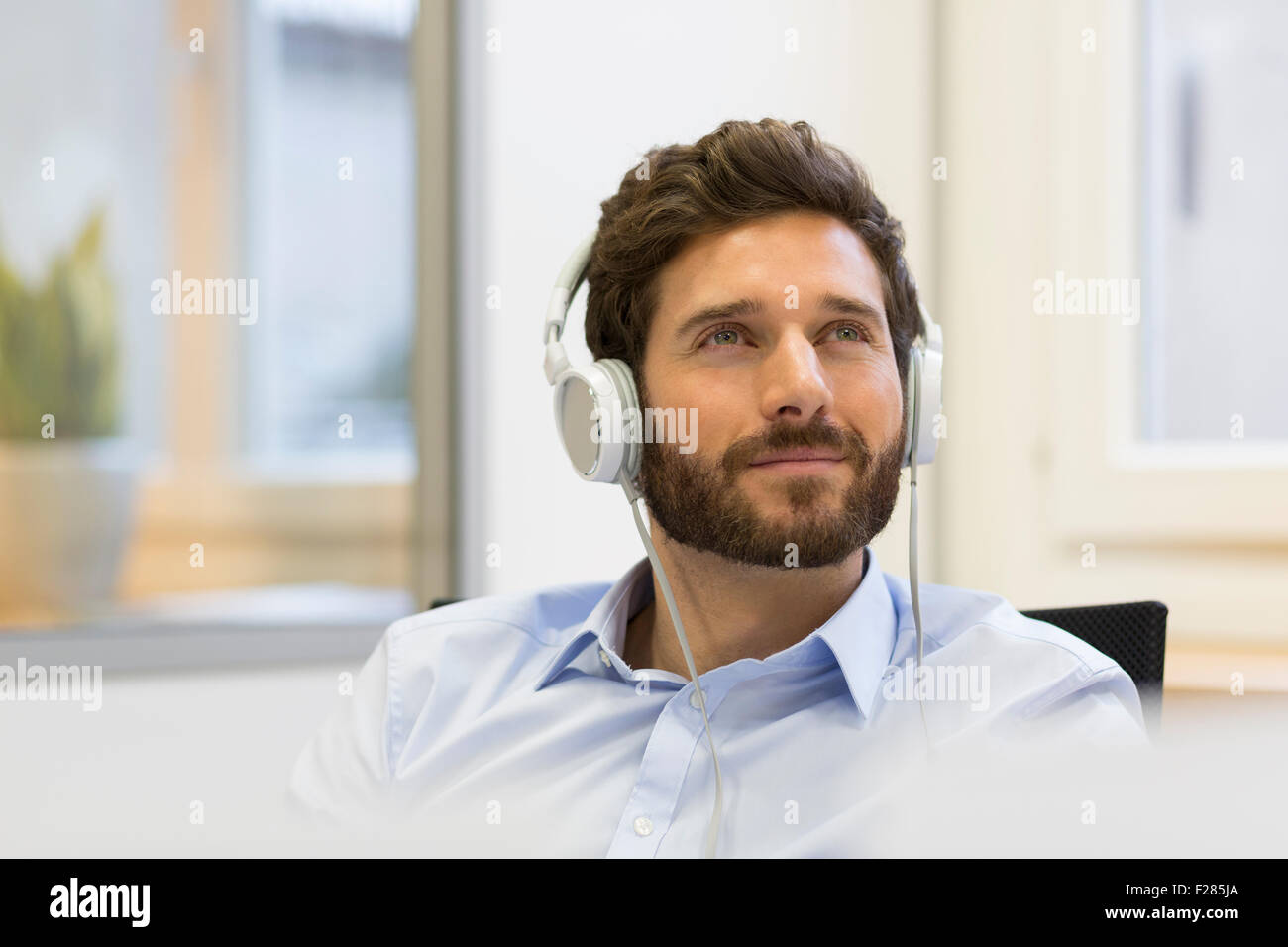 Empresario pensativo al escuchar música con auriculares Foto de stock