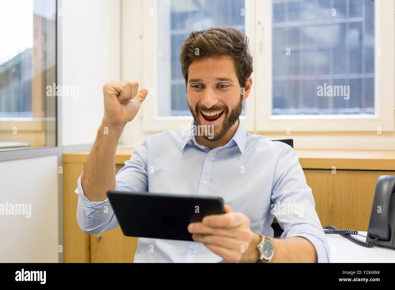 Empresario vítores con brazos arriba en Office mediante tableta digital Foto de stock