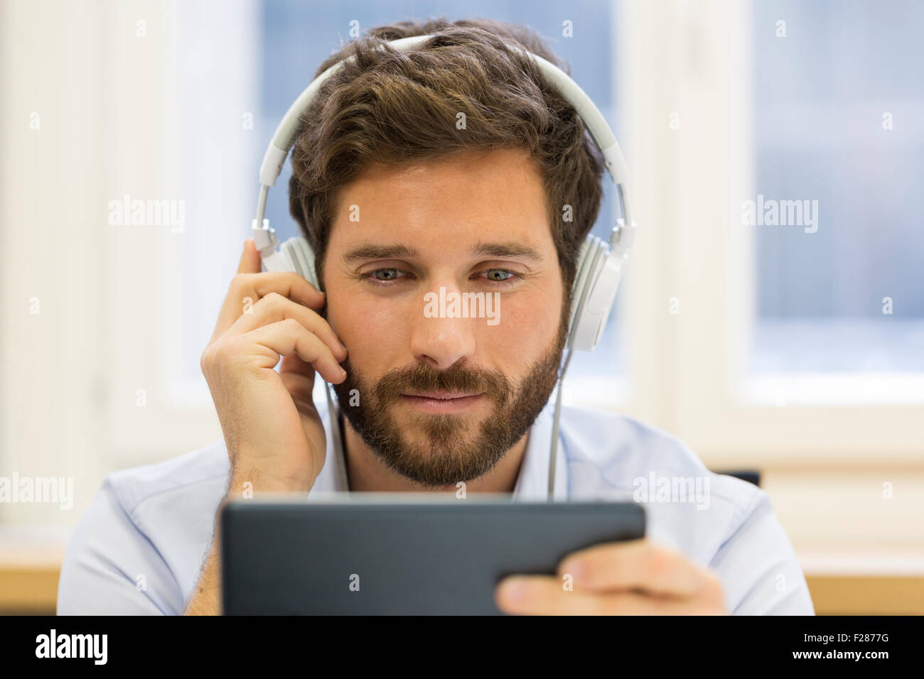 Empresario creativo escuchando auriculares y utilizando tablet digital. Foto de stock