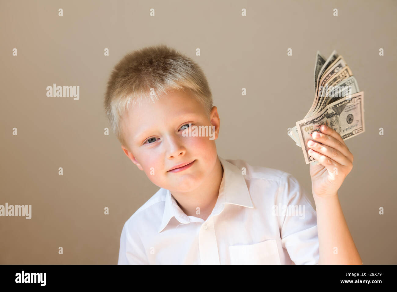 Feliz niño sonriente con dinero (dólares) en mano sobre fondo gris Foto de stock