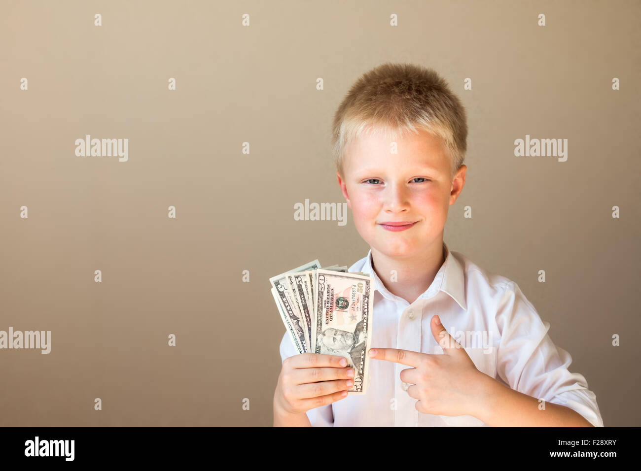 Feliz niño sonriente con dinero (dólares) en manos sobre fondo gris Foto de stock