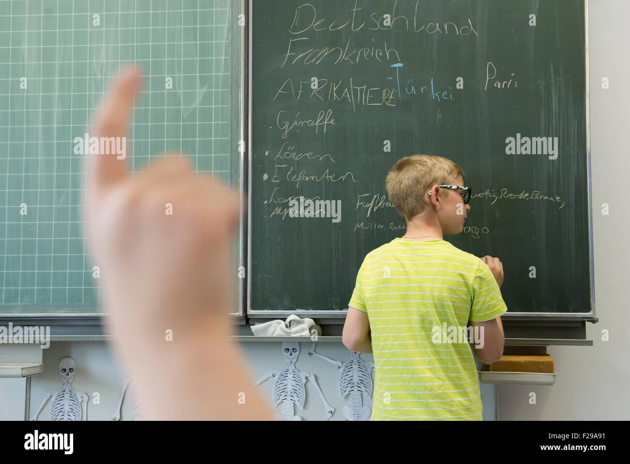 El colegial escrito sobre pizarra y una colegiala levantando la mano en el aula, Munich, Baviera, Alemania Foto de stock