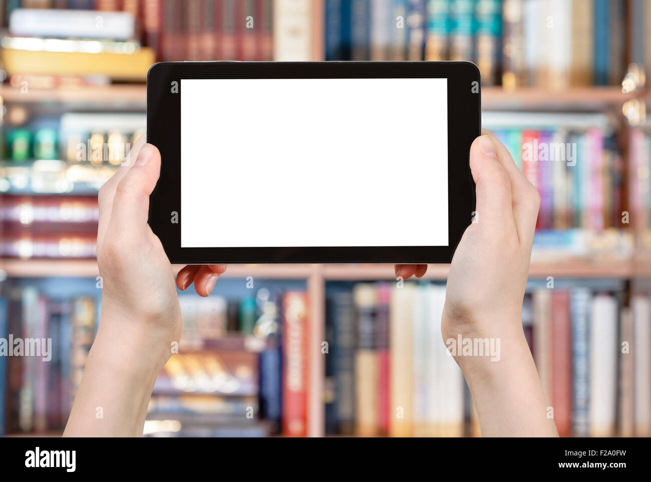 Manos sosteniendo tablet pc con pantalla recortada en la parte frontal de la biblioteca de libros Foto de stock