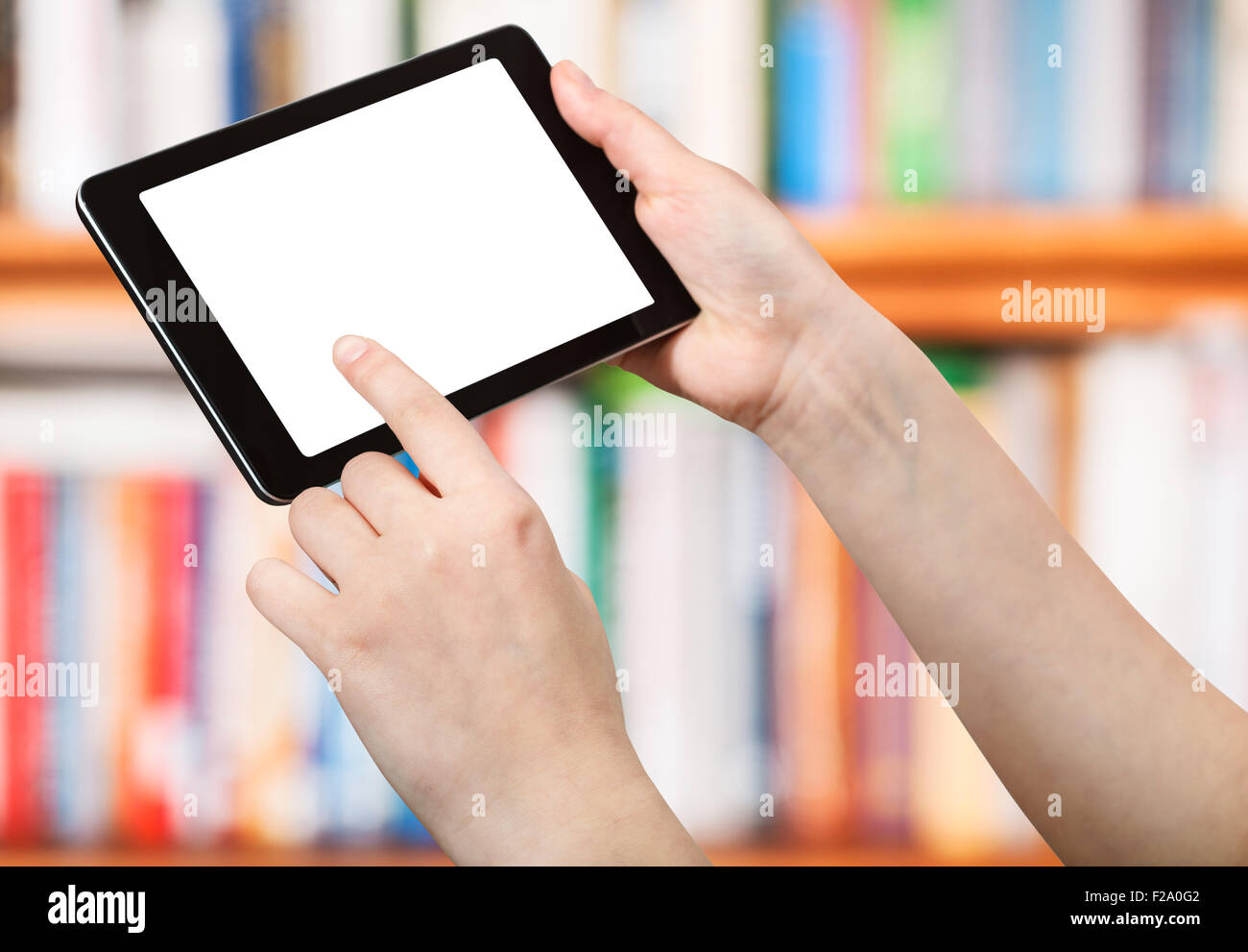Dedo toque tablet pc con pantalla de corte en la parte delantera de estantes de libros Foto de stock