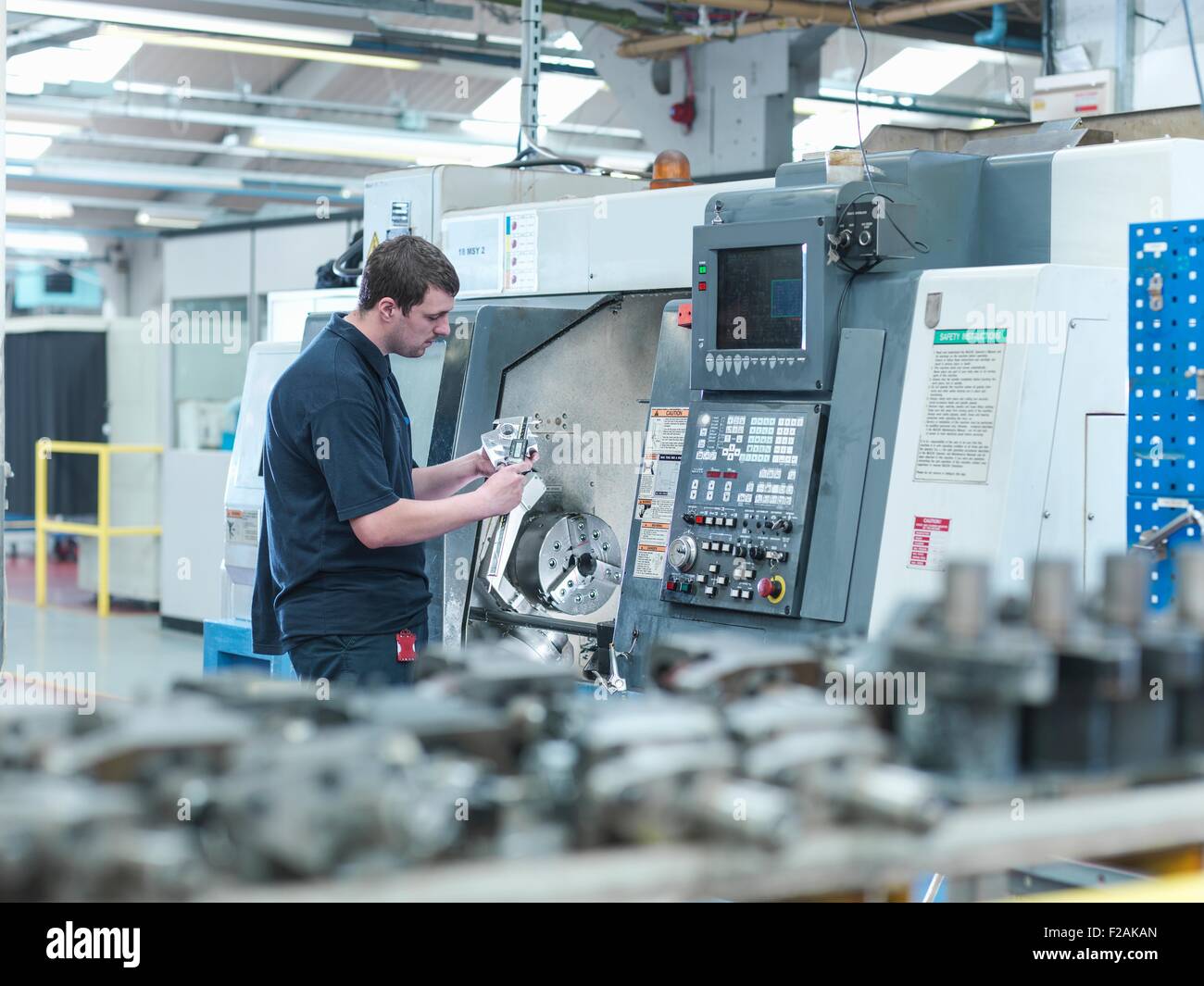 Trabajador masculino inspección de piezas en torno CNC en fábrica de ingeniería Foto de stock
