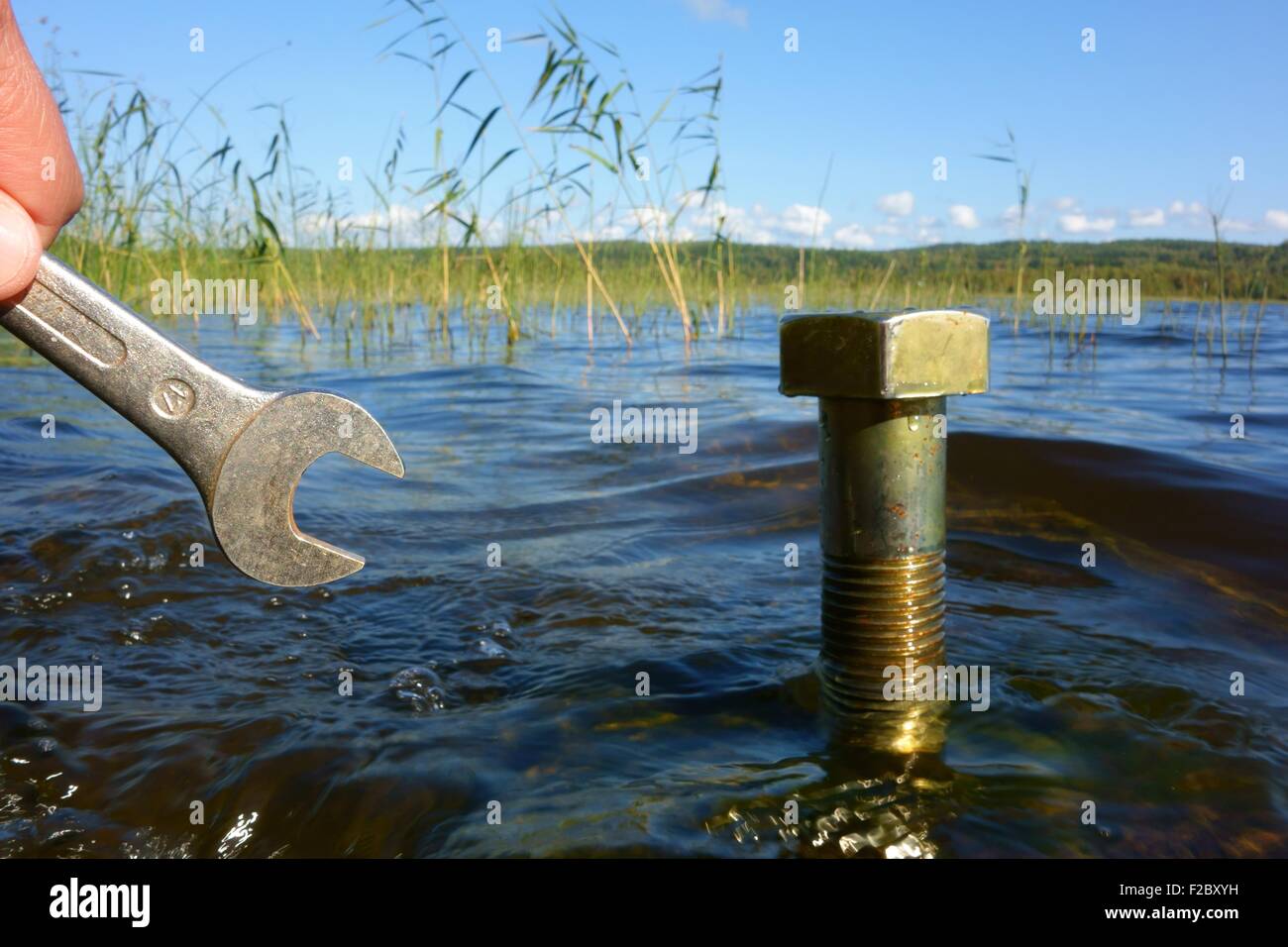 Concepto de protección del agua: par de dedos color plata holding instrumento al lado de un gran tornillo metálico derivadas del agua del lago. Foto de stock