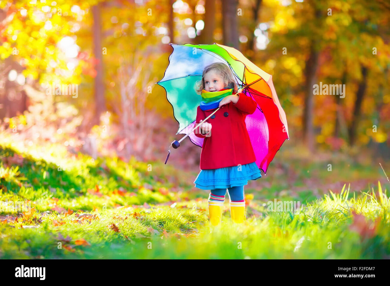 Niña jugando en la lluvia en otoño del parque. Niño sosteniendo paraguas caminando en el bosque en un soleado día de otoño. Foto de stock