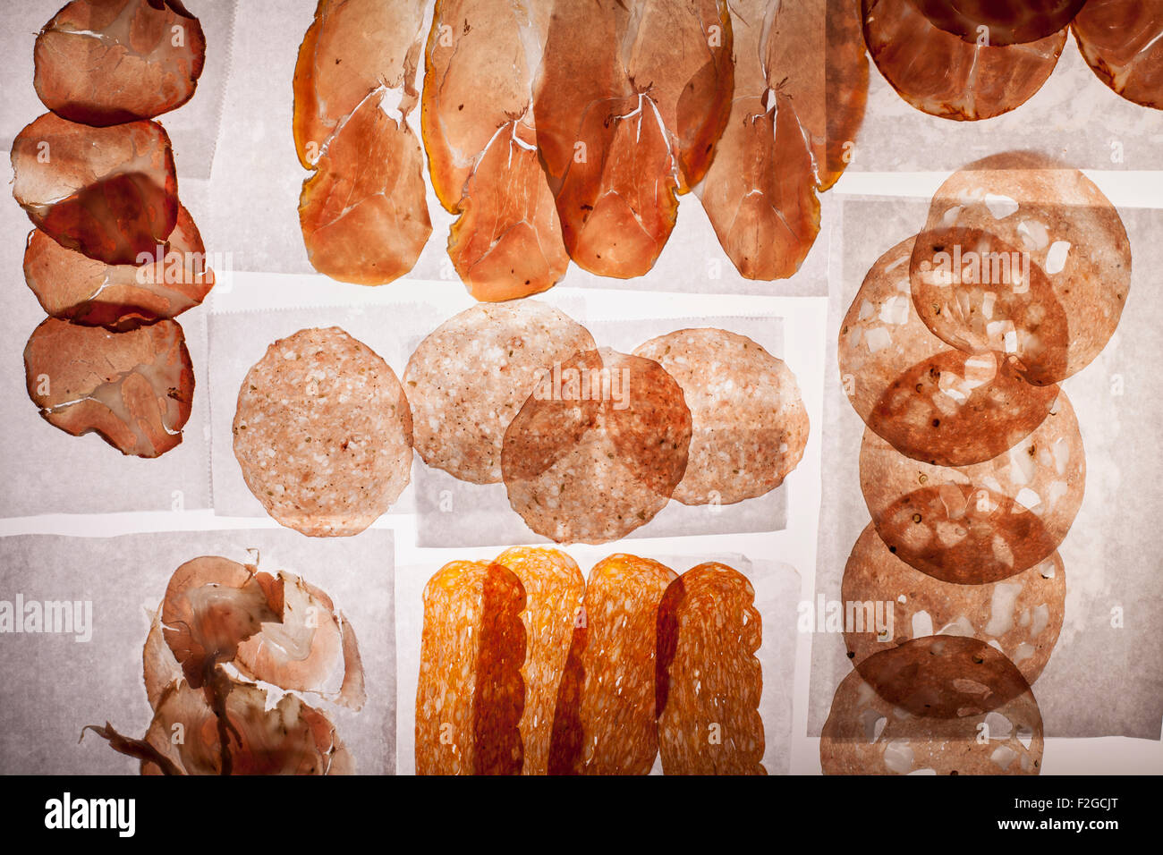 Cortes translúcidas de diversos salami y jamón sobre blanco deli papel encendido en la mesa de luz Foto de stock