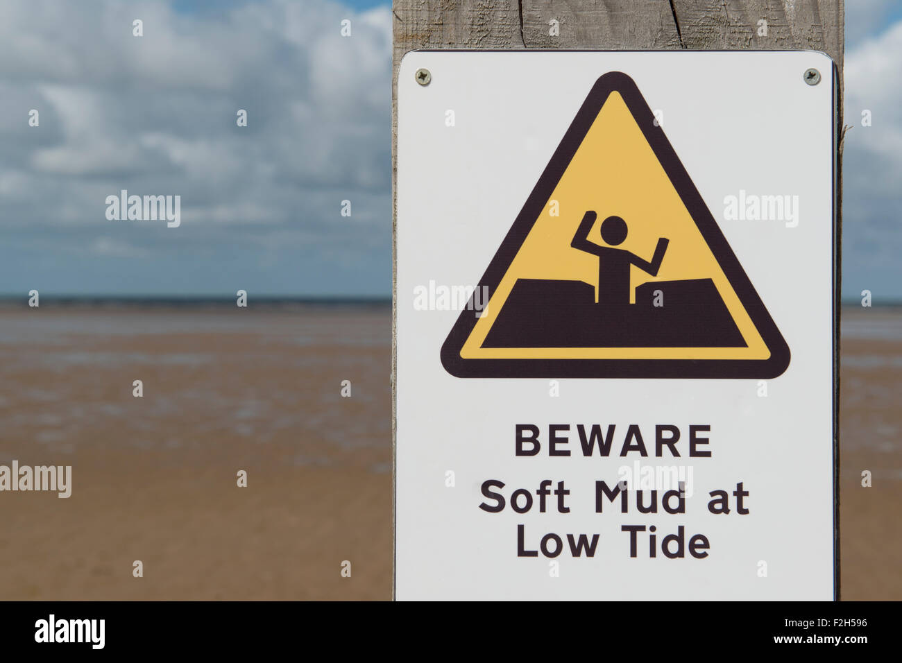 Un signo de advertencia de lectura Cuidado con barro blando con marea baja en una playa cerca de Prestayn en Gales. Foto de stock