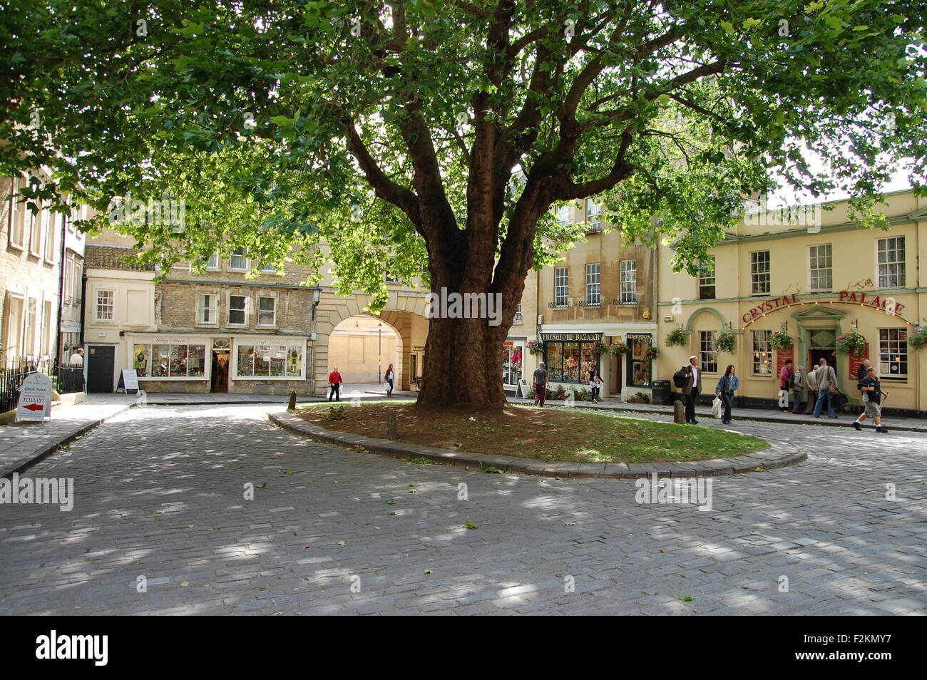 Plaza adoquinada y tiendas a la sombra de un árbol grande en Abbey verde en la ciudad de Bath, Inglaterra Foto de stock