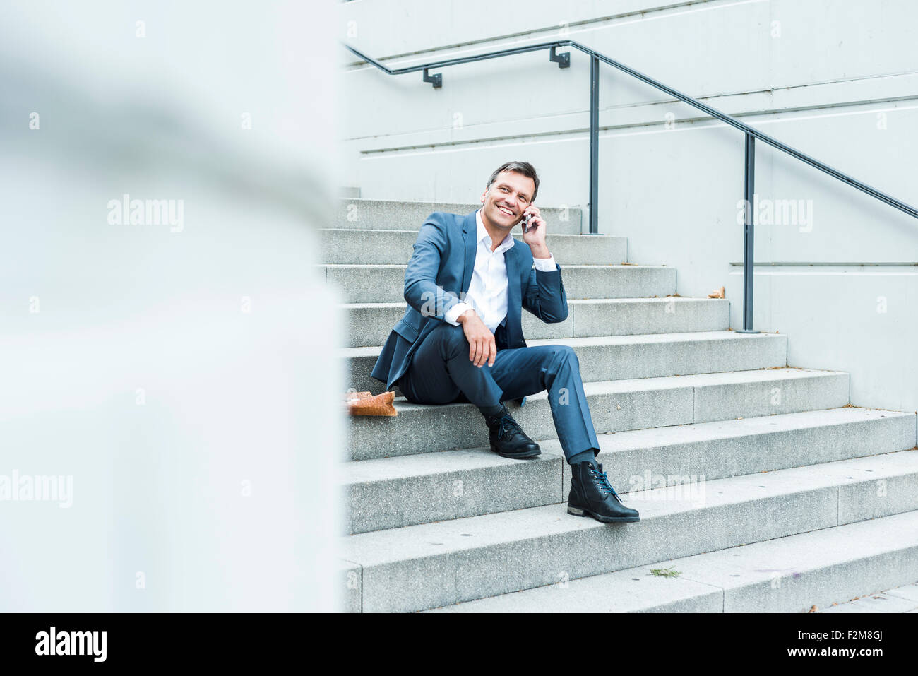 Empresario sentado en las escaleras con teléfonos inteligentes. Foto de stock