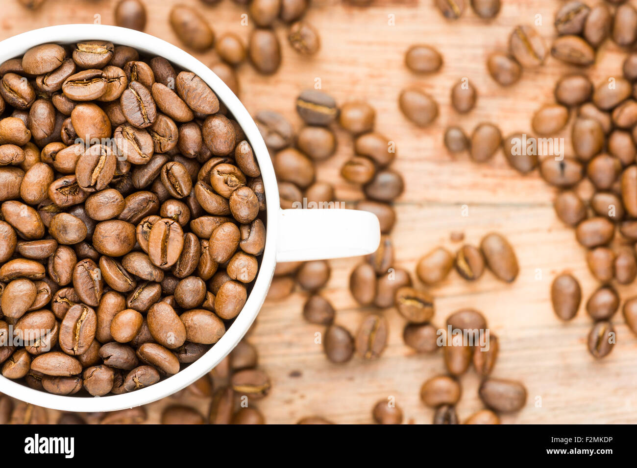 Los granos de café dentro de mitad blanca visible taza sin placa sobre fondo de madera aislado Foto de stock