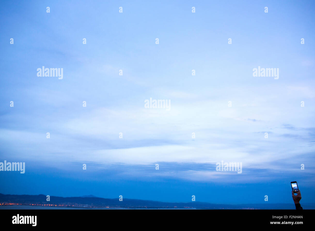 Mano sujetando celular bajo el cielo crepuscular Foto de stock