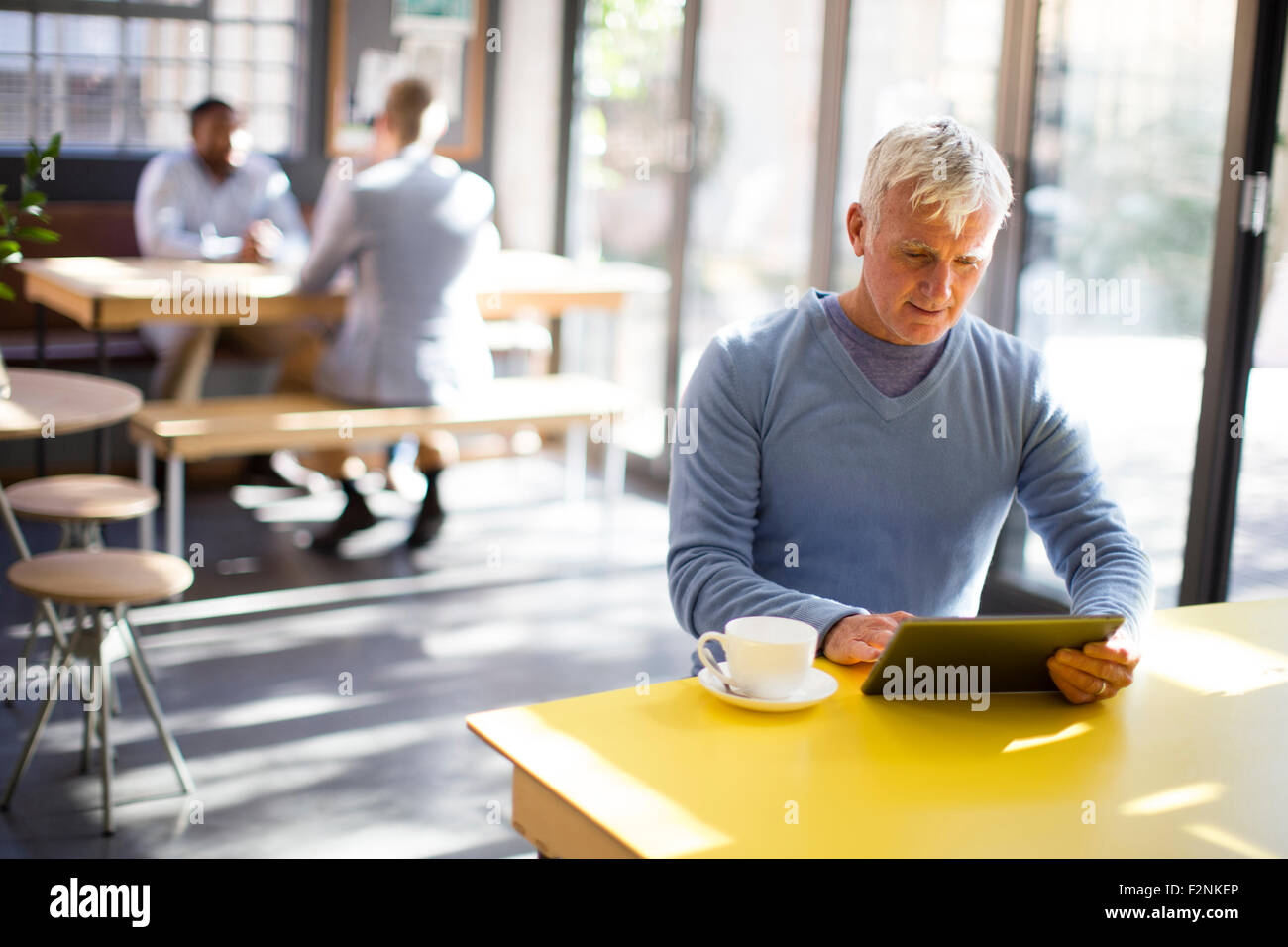 Hombre de edad avanzada utilizando digital comprimido en cafe Foto de stock