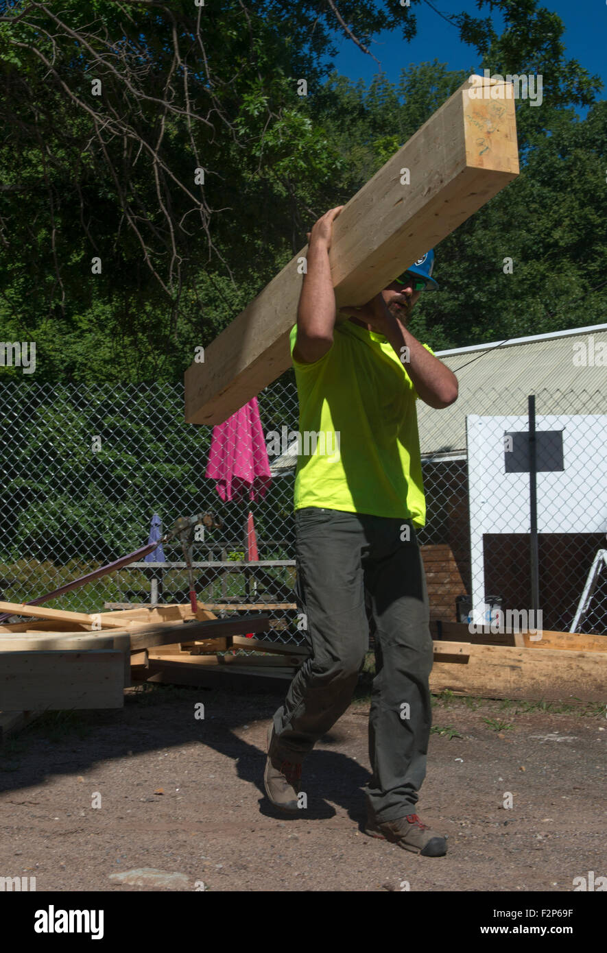 Trabajador de la construcción lleva la viga para la instalación en el nuevo edificio de la escuela Hight terreno común. Foto de stock