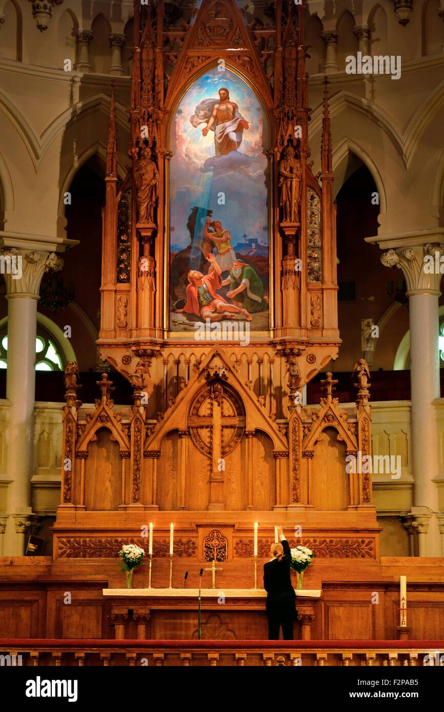 Helsinki, Finlandia. La Iglesia Luterana Finlandesa Johanneksenkirkko de San Juan retablo interior. Mujer encendiendo velas de altar Foto de stock