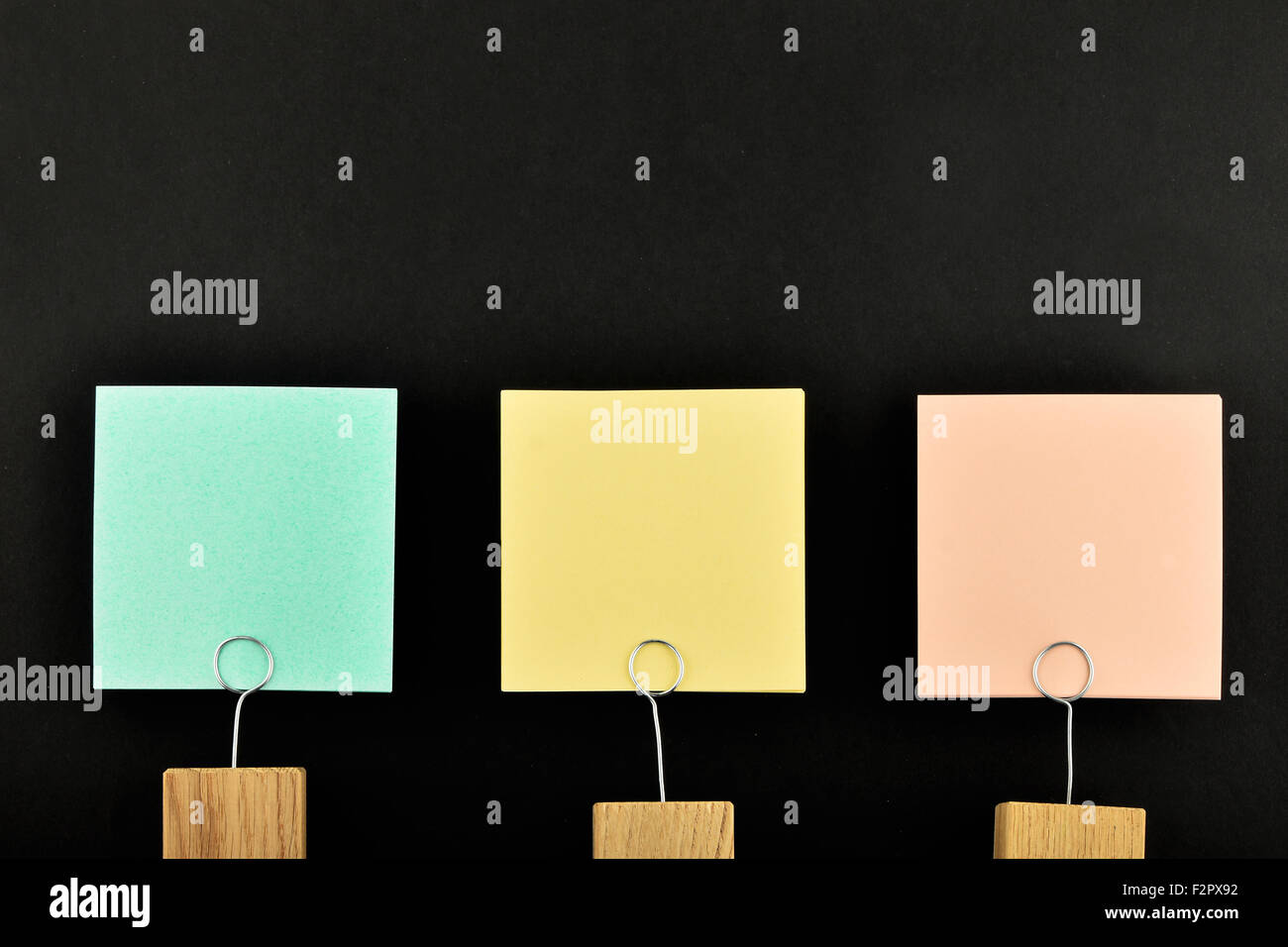 Tres notas de papel, verde, amarillo, rosa, con soporte de madera aislado en papel negro de fondo para la presentación Foto de stock