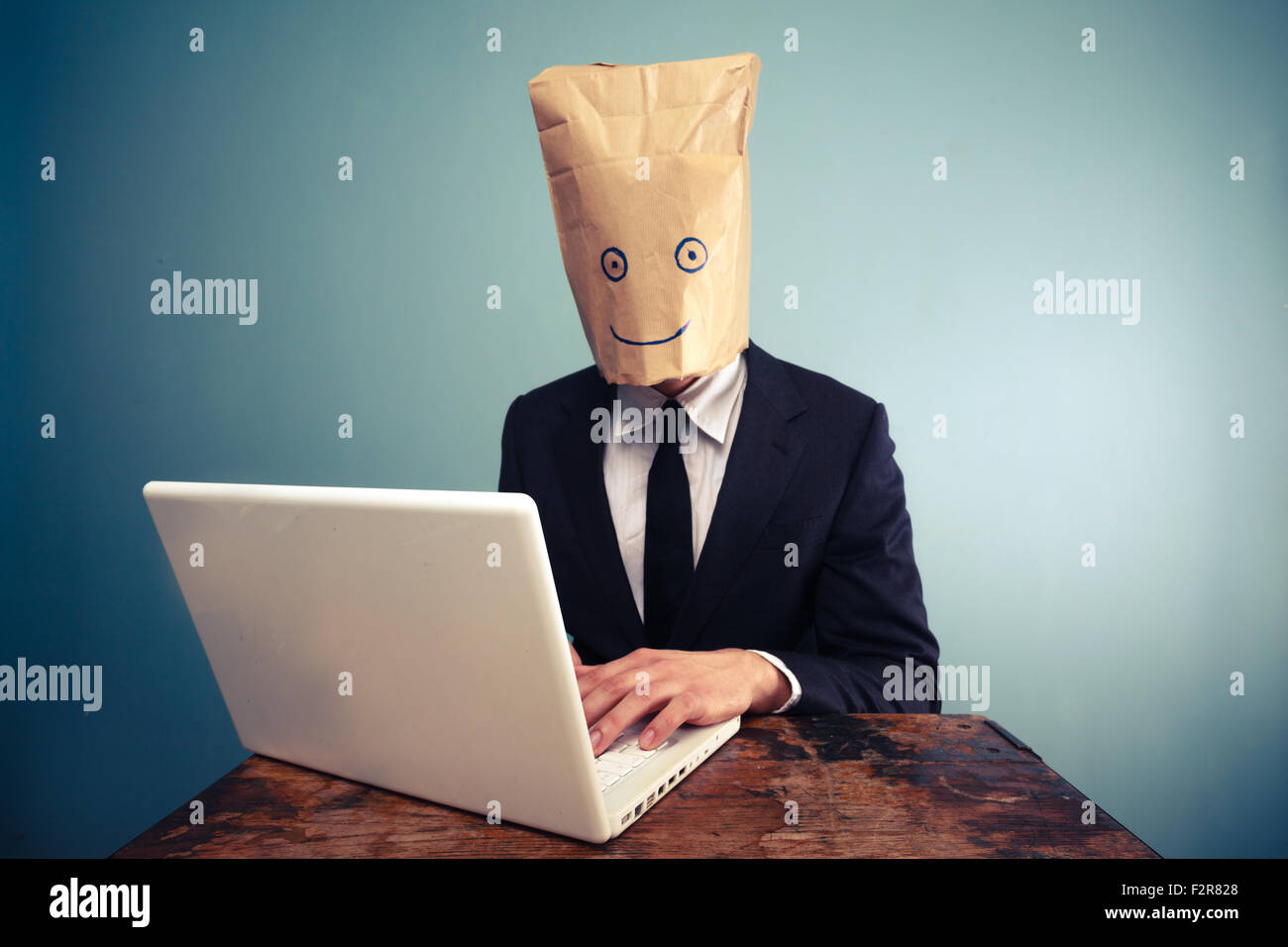 feliz-empresario-con-una-bolsa-de-papel-sobre-su-cabeza-esta-utilizando-un-equipo-portatil-f2r828.jpg
