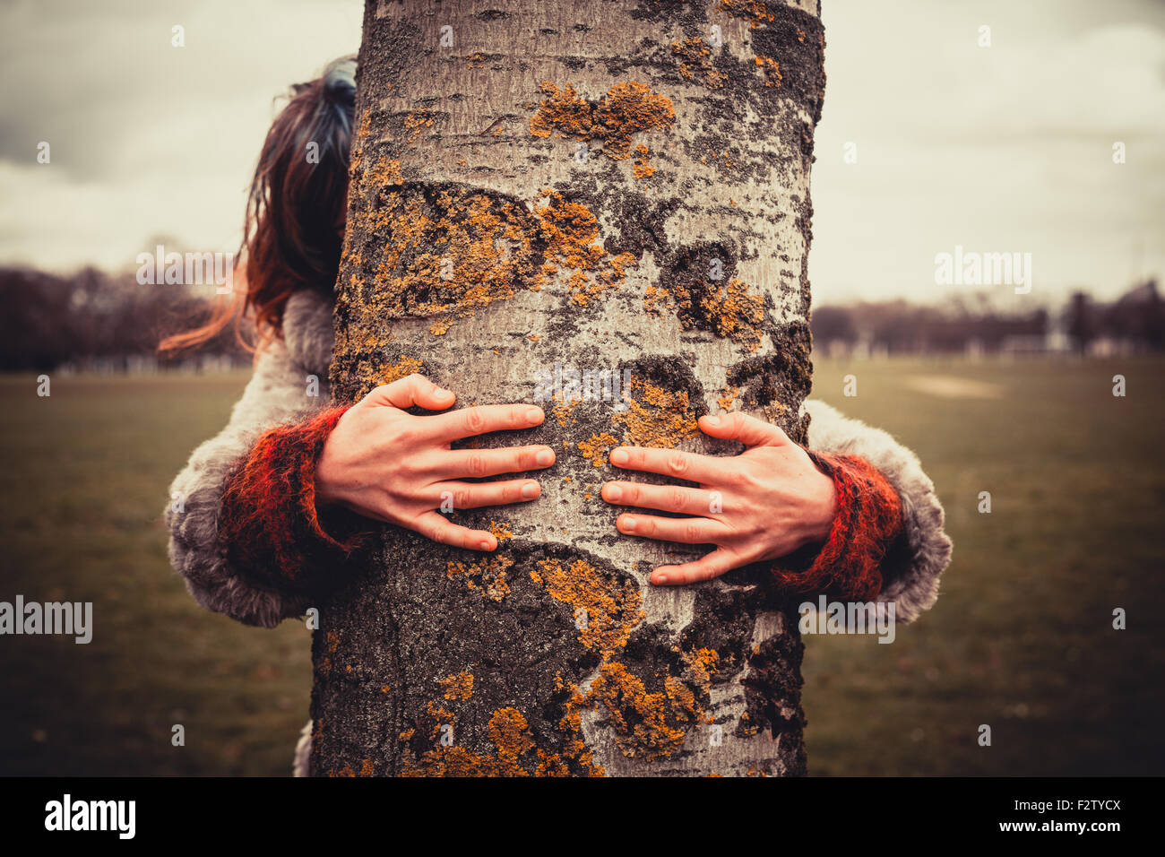 Mujer joven está en el parque en un día de invierno y está abrazando un árbol Foto de stock