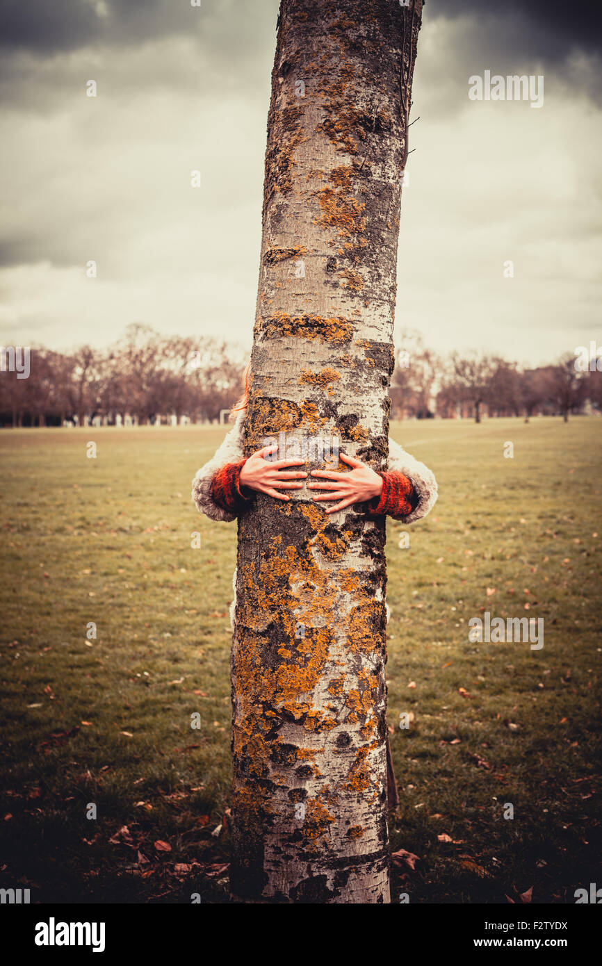 Mujer joven está en el parque en un día de invierno y está abrazando un árbol Foto de stock