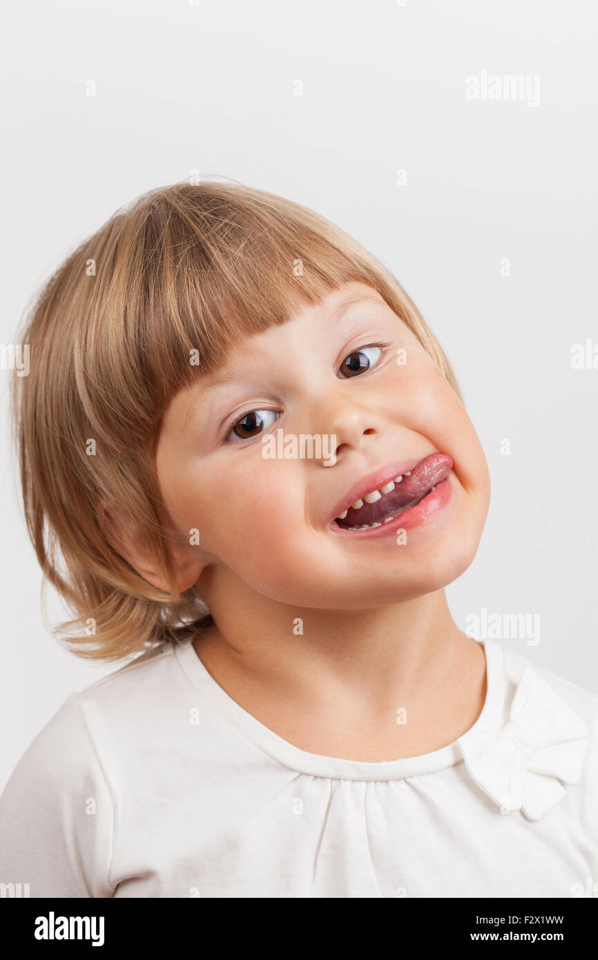 Cute Little Girl muestra lengua caucásica, closeup studio retrato sobre fondo gris claro Foto de stock
