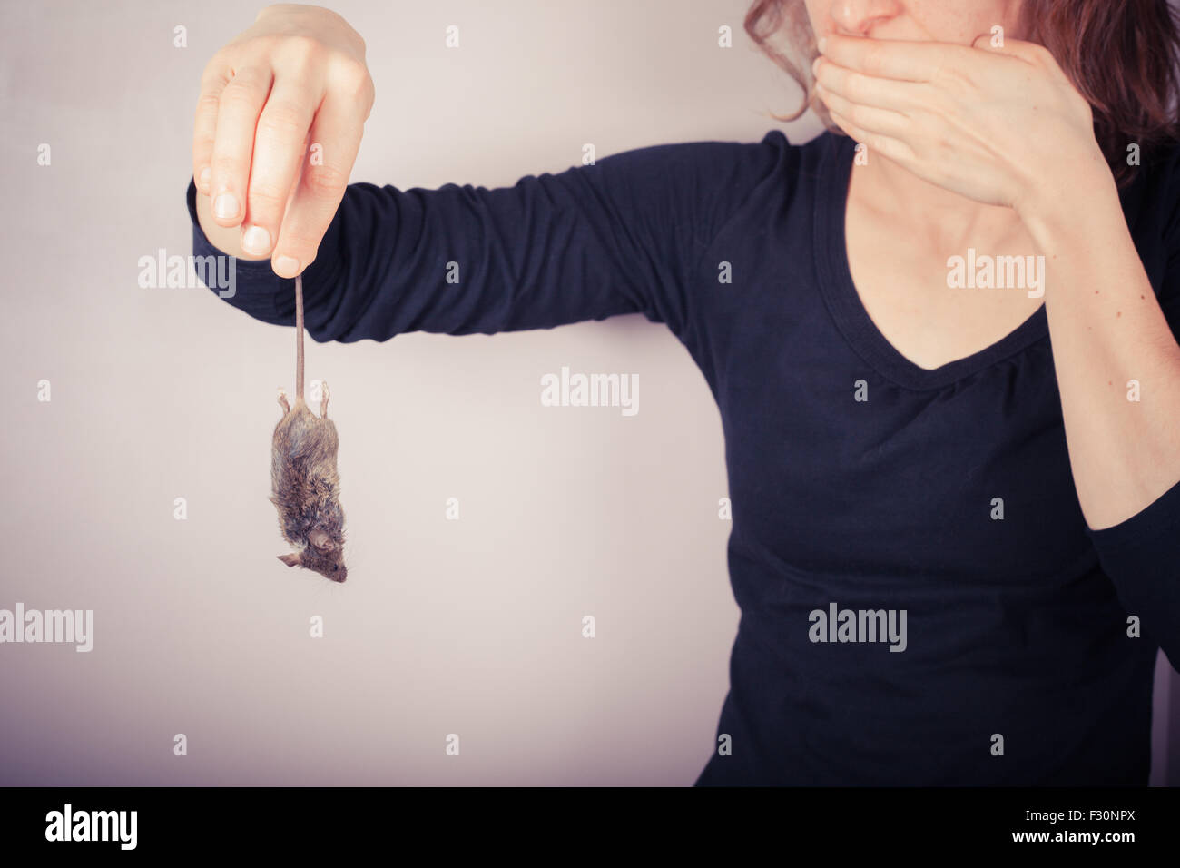 Un aprensivo y disgustados mujer sosteniendo un ratón muerto por su cola Foto de stock