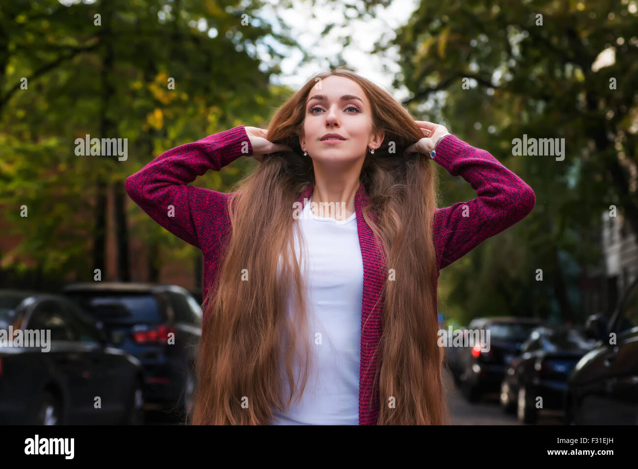 Hermosa mujer joven en violeta chaqueta con pelo largo parado en el verde  de las calles de la ciudad con coches borrosa en ambos lados Fotografía de  stock - Alamy