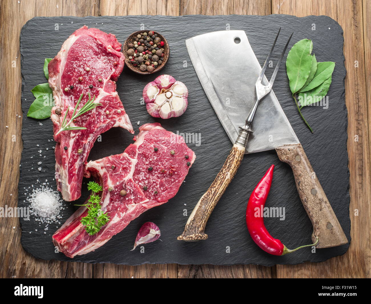 Filetes de carne cruda con especias sobre negro tabla de cortar. Foto de stock