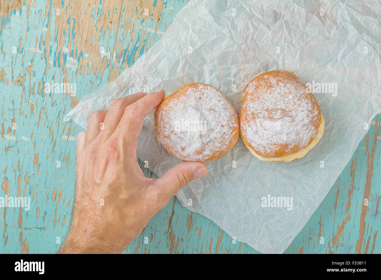 Hombre mano alcanza y recogiendo dulces donut azucarado de mesa de cocina de madera rústica, deliciosa panadería donuts Fotografía cenital Foto de stock