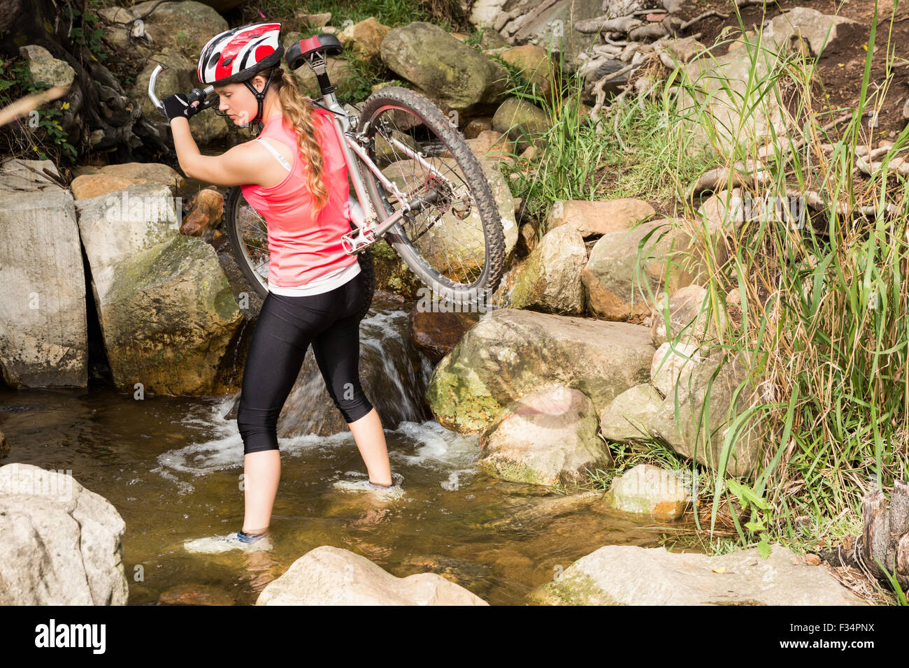 Atleta rubia llevando su bicicleta de montaña a través de stream Foto de stock