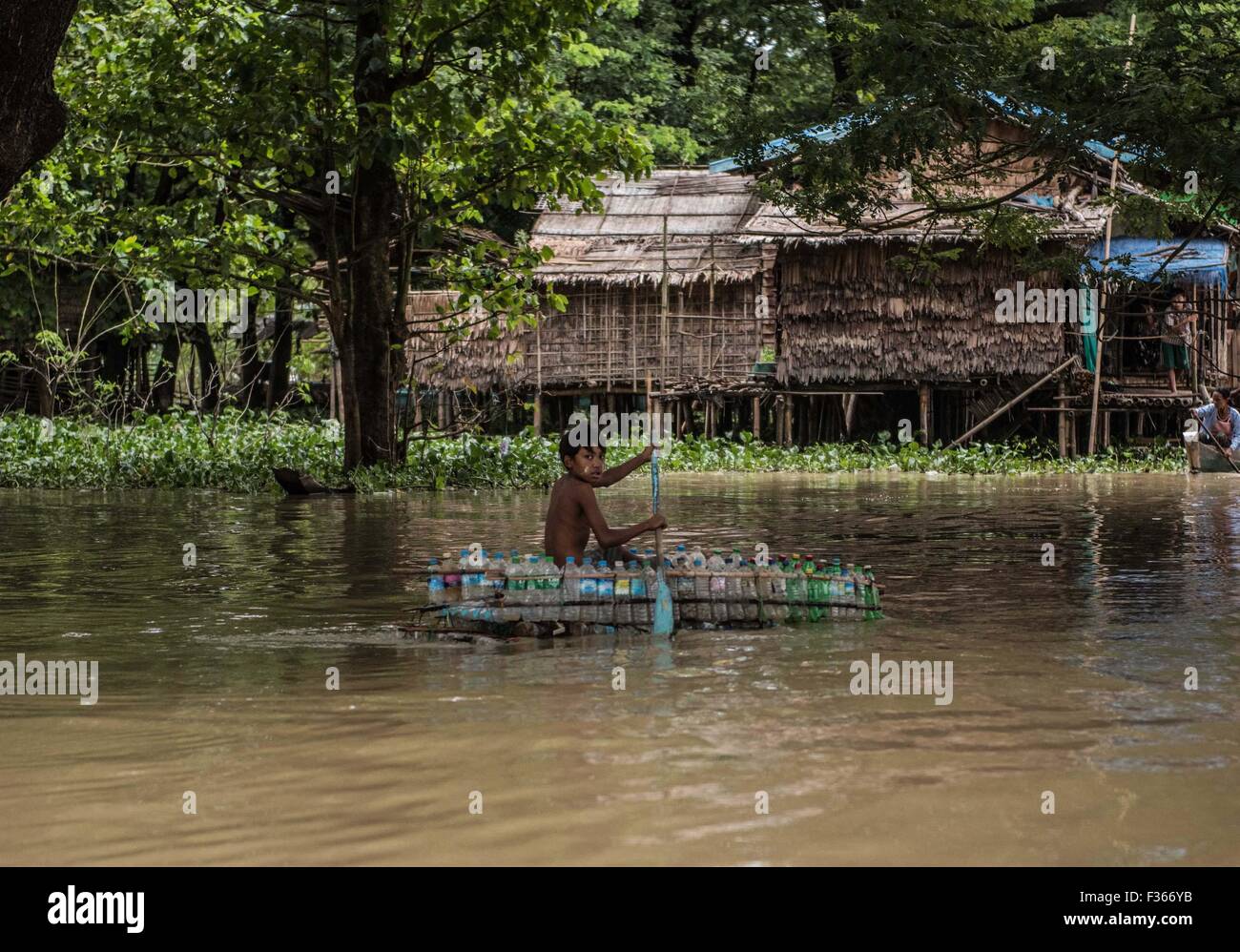 Un muchacho remos un barco hecho de botellas de plástico recicladas en una villa inundada en la región del delta del Irrawaddy, en Myanmar. Foto de stock