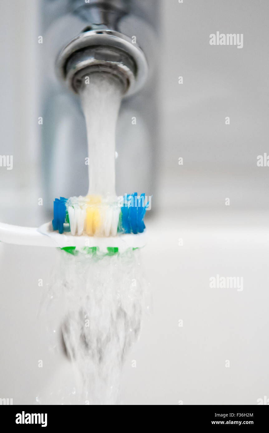 Cepillo de dientes se enjuaga bajo el grifo de agua de un grifo Foto de stock