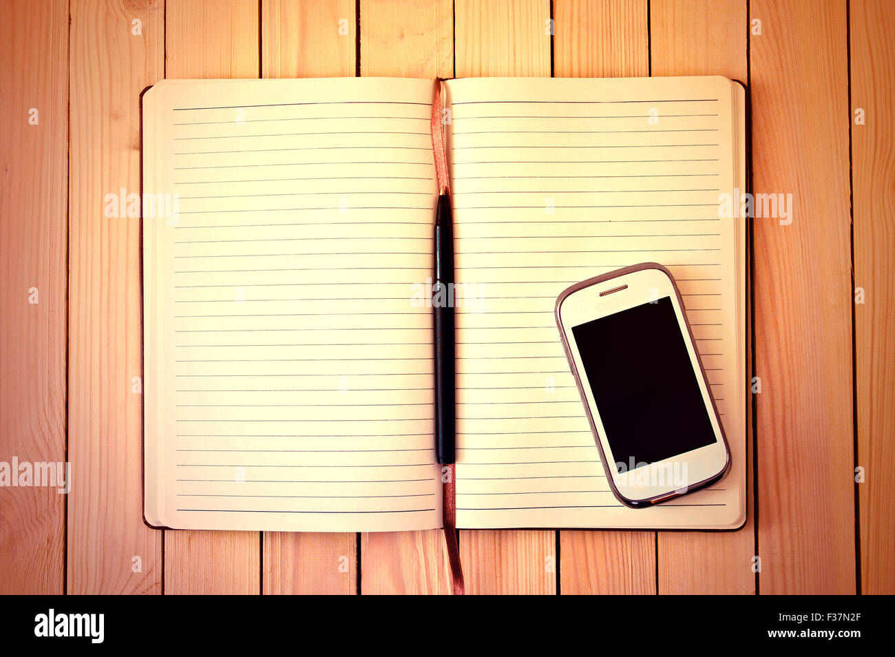 Teléfono celular blanco, una pluma y un cuaderno en la mesa de madera. Espacio de trabajo. Foto de stock