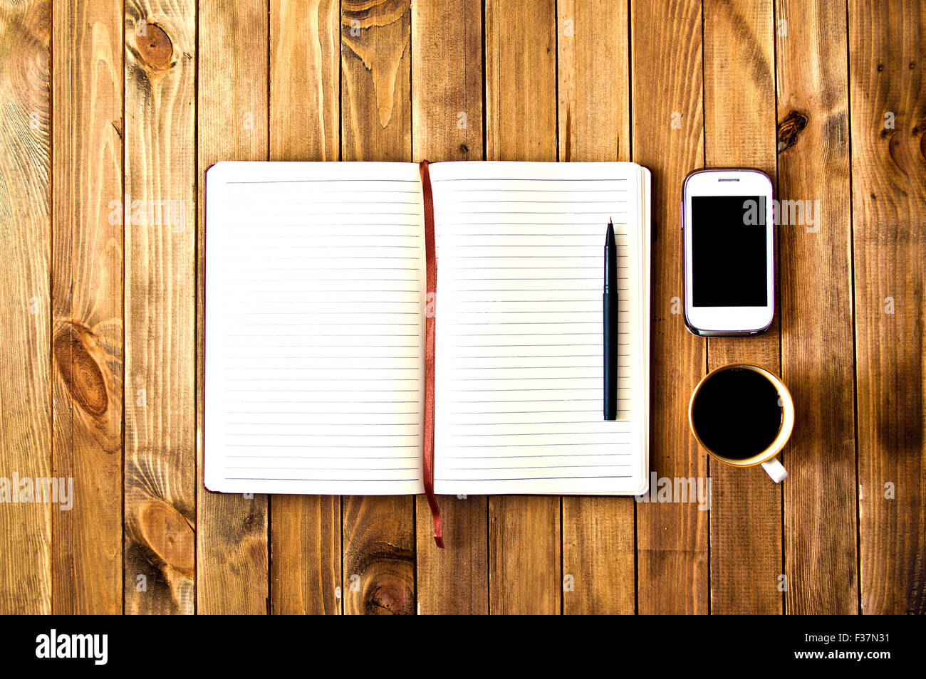 Teléfono celular blanco, un bolígrafo, una taza de café y el portátil en la mesa de madera. Espacio de trabajo. Vintage Instagram fotografía. Foto de stock