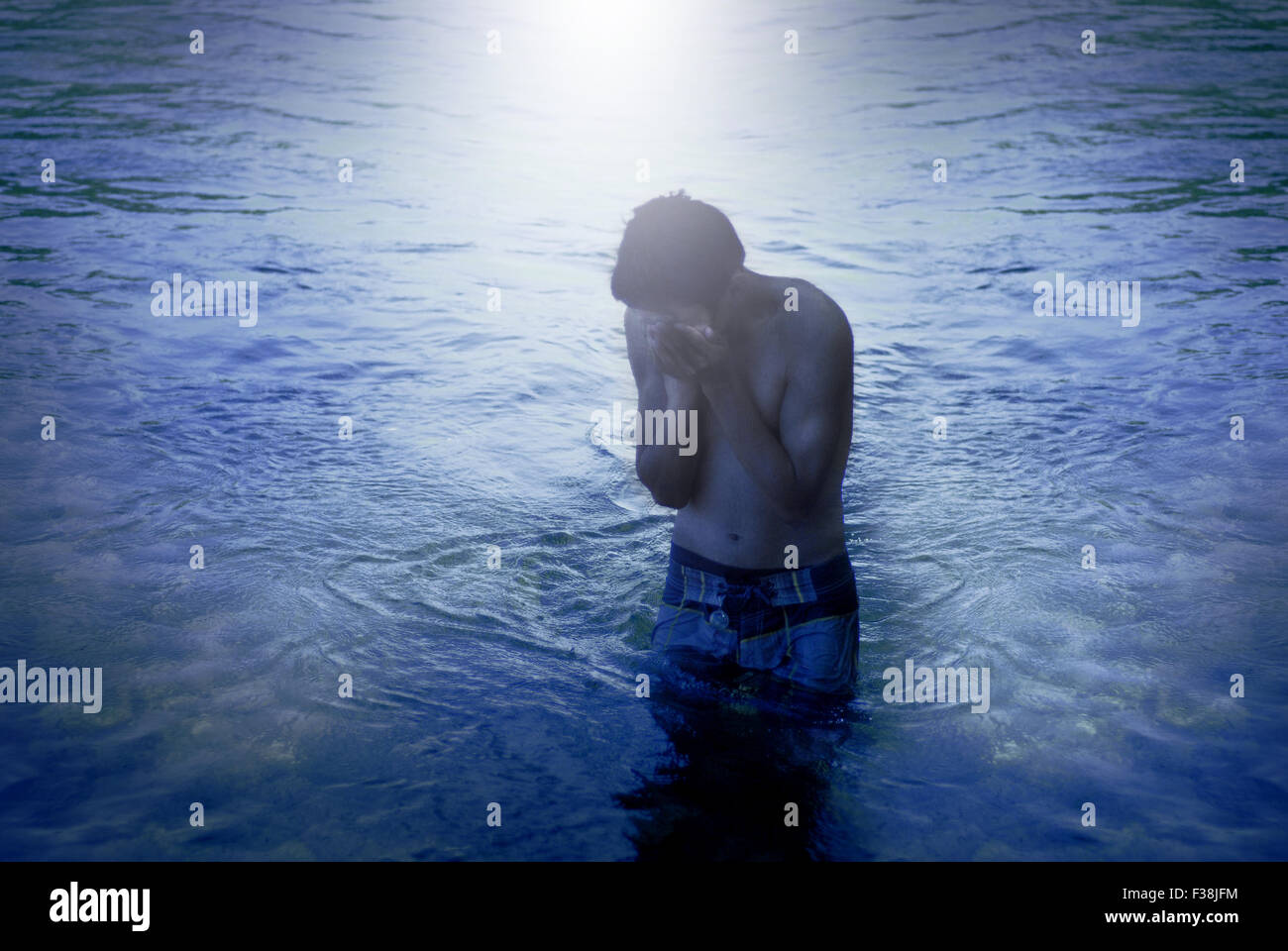 Joven que cubre su rostro en el agua, la luz blanca Foto de stock