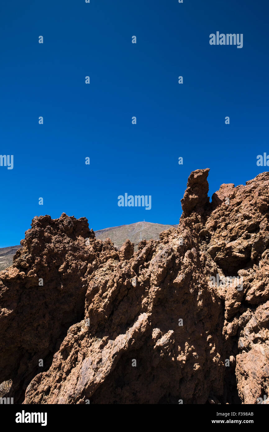 Jagged rocas volcánicas en primer plano con las torres del cablecarril visibles en las laderas del Teide detrás, en el ámbito nacional Foto de stock
