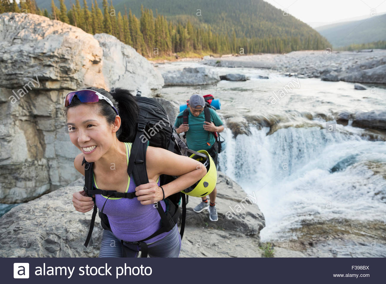 Mujer sonriente caminante con mochila cerca escarpada cascada Foto de stock