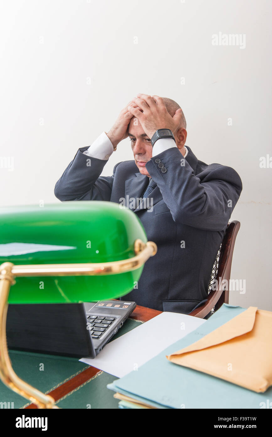 Un hombre de negocios agonizante, en crisis, delante de su PC. En su estudio, a solas con su desesperación y su pánico. Foto de stock