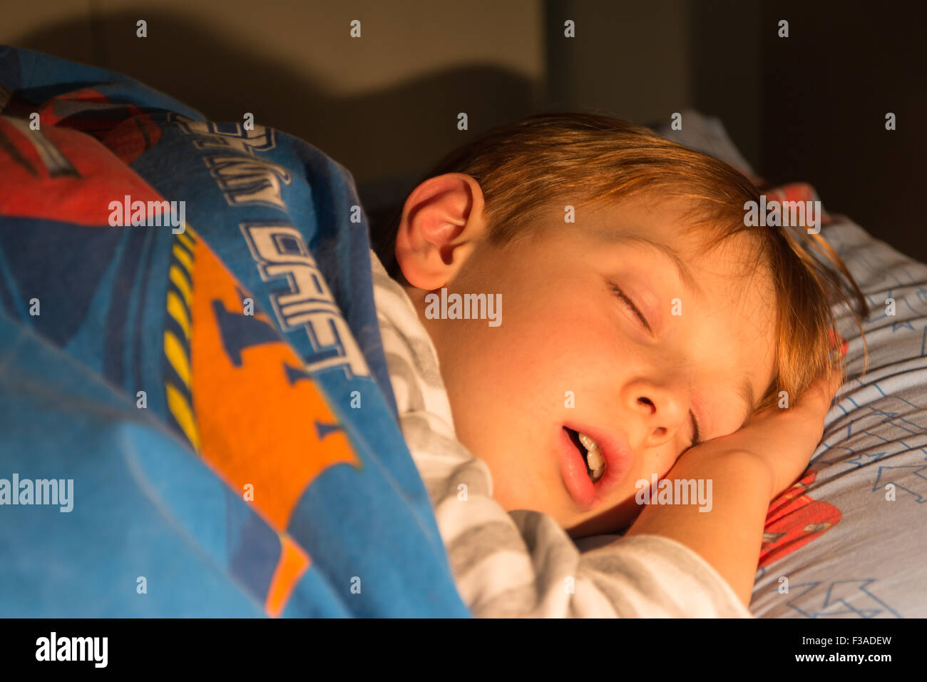 Niño de 8 años duerme en la cama con un edredón Foto de stock