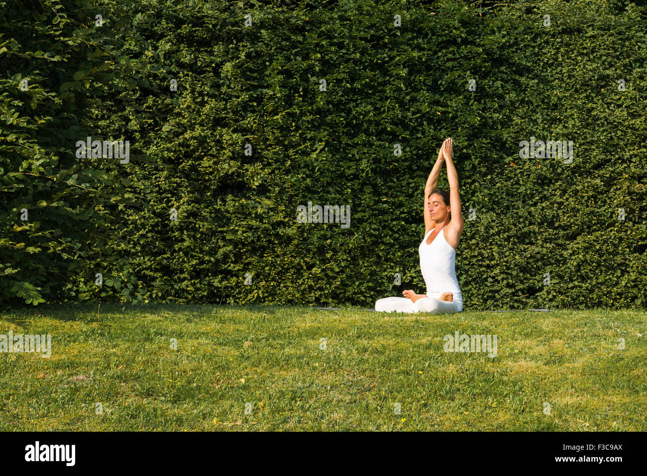 Mujer joven, vistiendo un traje de cuerpo blanco, es practicar el Hatha-yoga piscina entre árboles, mostrando la pose: padmasana, lotus plantean Foto de stock