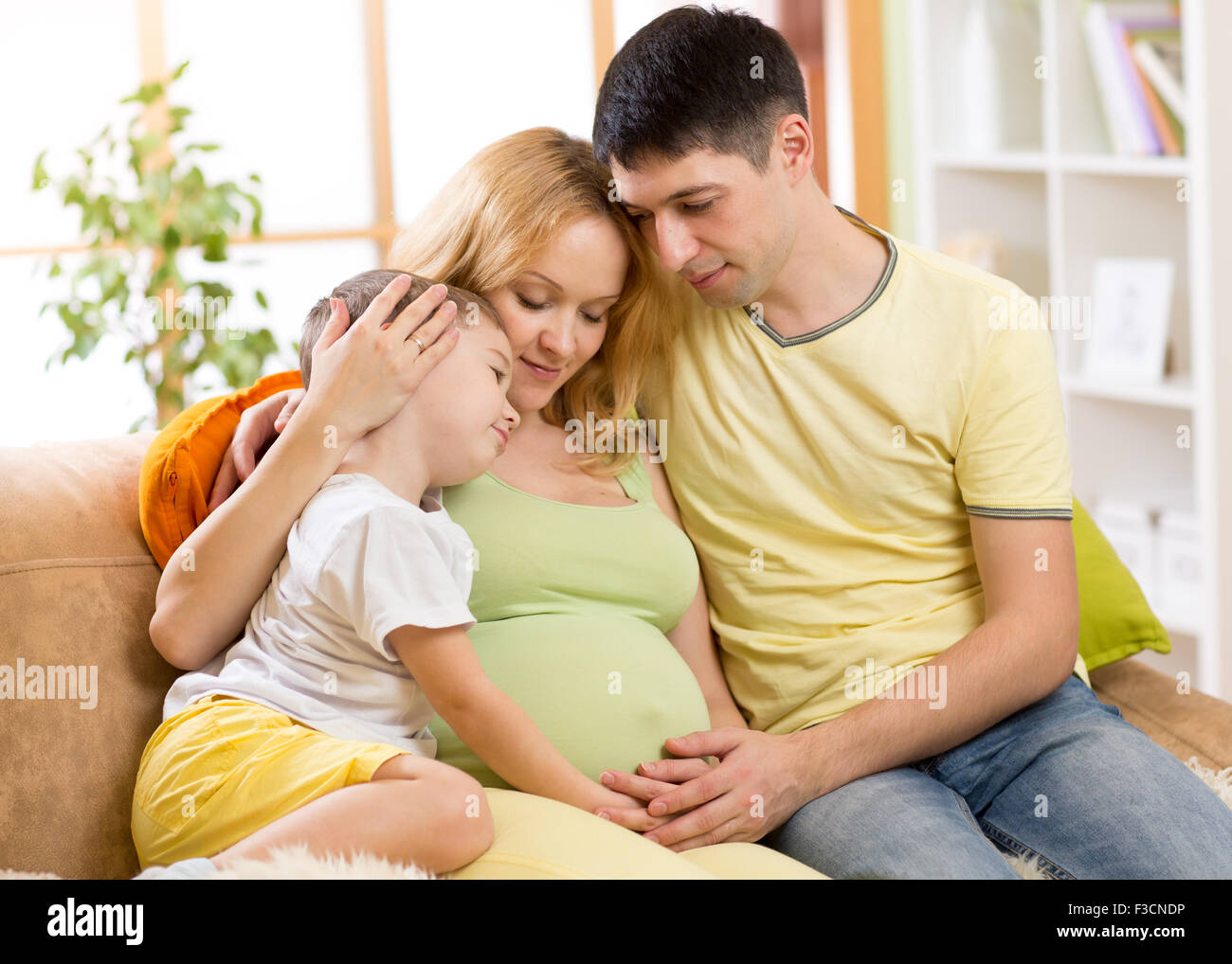 Familia Feliz en previsión del nacimiento del nuevo bebé. La mujer embarazada y el marido en el sofá en casa Foto de stock