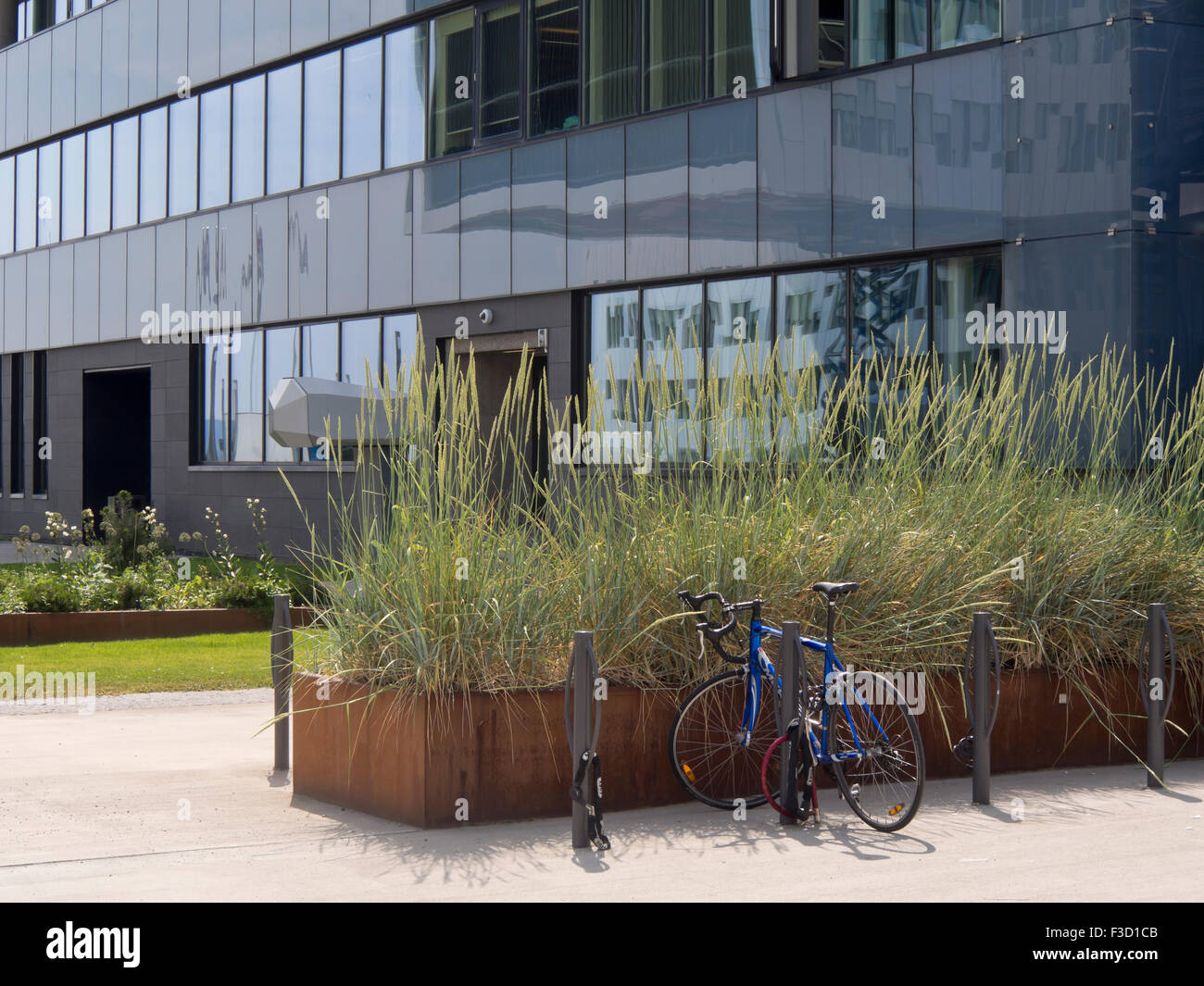 Soporte para bicicletas fuera moderno y elegante edificio de oficinas para ciclismo fácil conmutar, rusty maceta de flores y hierbas onduladas Oslo Noruega Foto de stock