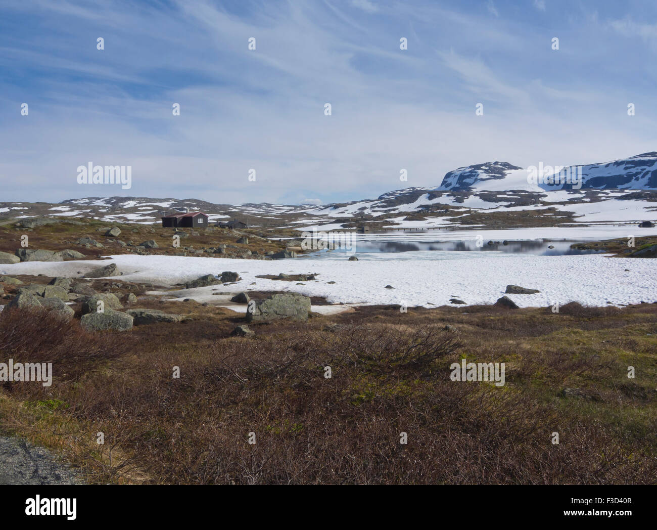 Vista panorámica de las montañas noruegas, cabaña, Lago, parches de nieve y glaciares lejanos, Hardangervidda Finse, Noruega Foto de stock