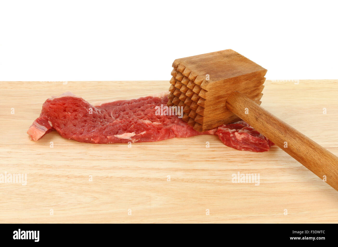 Solomillo con un martillo de carne sobre una tabla de madera sobre un fondo blanco. Foto de stock