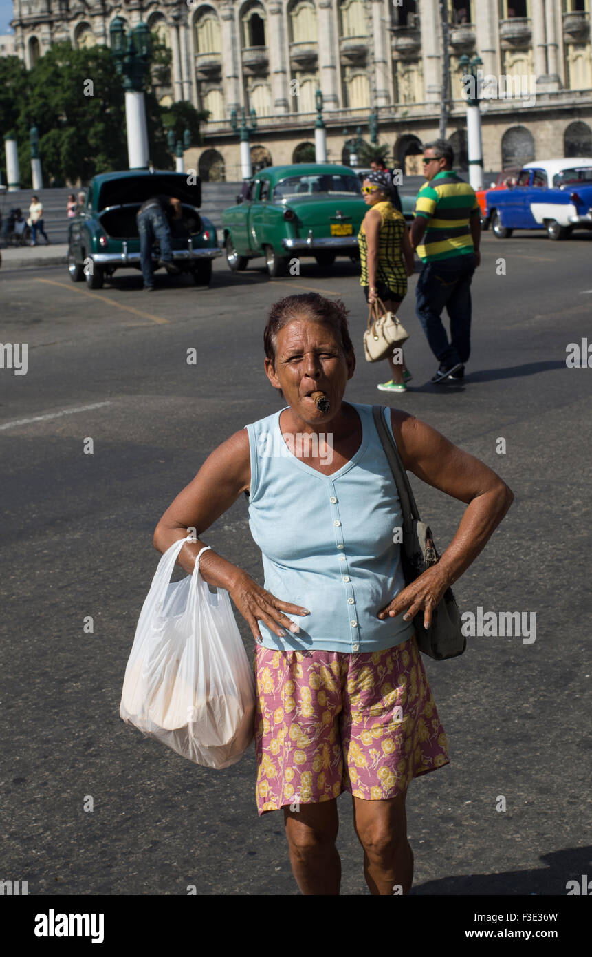 Una mujer local representa las manos en las caderas con sus compras de fumar un cigarro cubano sonriente en La Habana, la capital de la República de Cuba Foto de stock